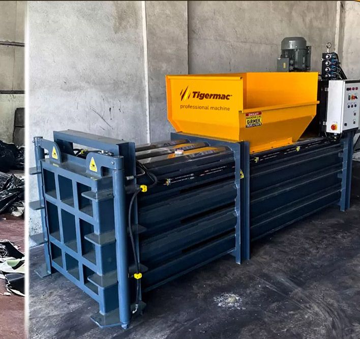 Tigermac bale press machine with a yellow hopper in a recycling facility