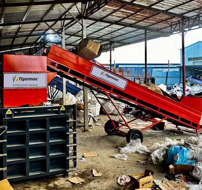 Red Tigermac inclined belt conveyor feeding a bale press
